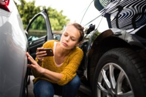 A woman looking at a dent in the side of her car, wondering how to tell who sideswiped who.