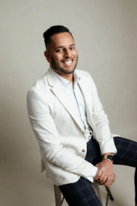 Photo of H&P Law’s new team member, Arun, sitting on a stool and smiling into the camera.