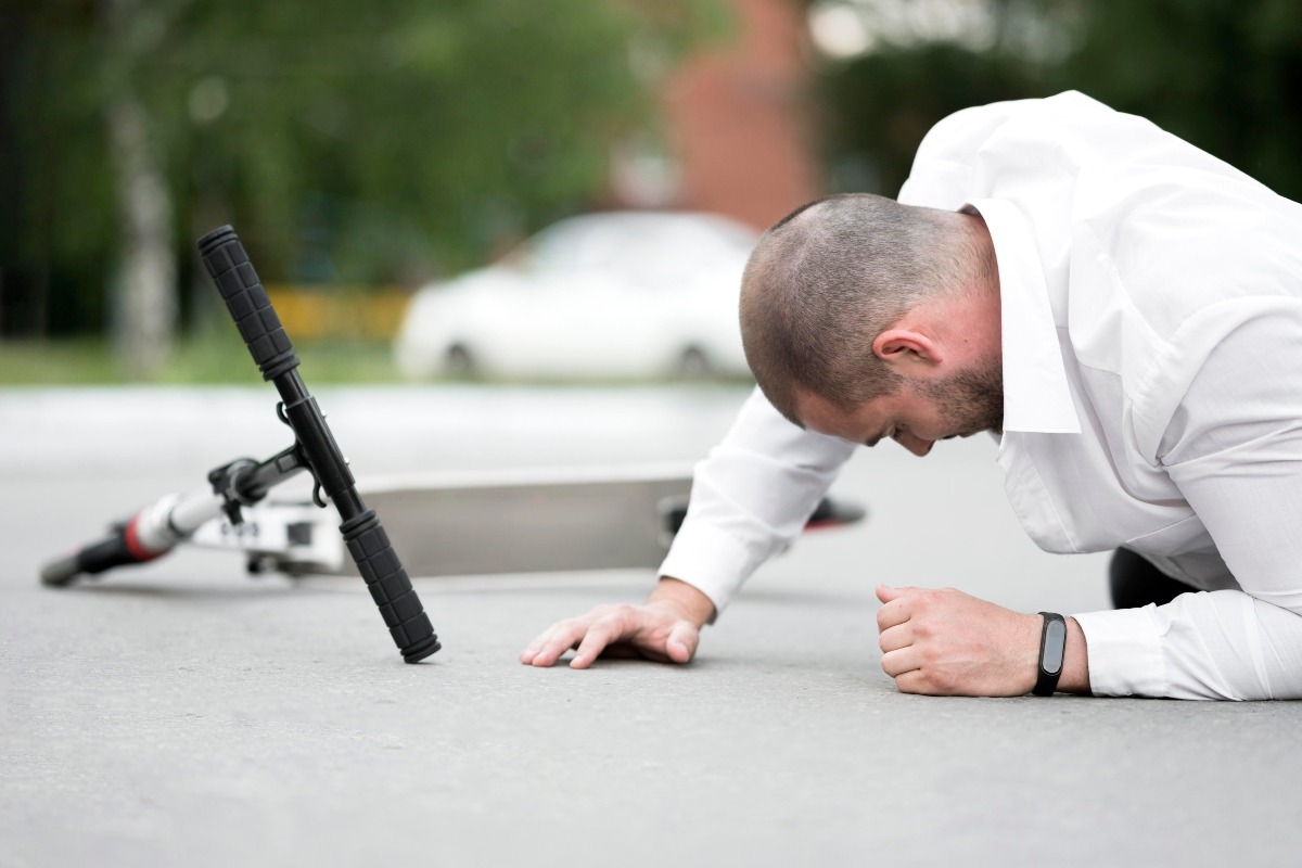 A man lying on the street next to his scooter after he’s been hit by a car.