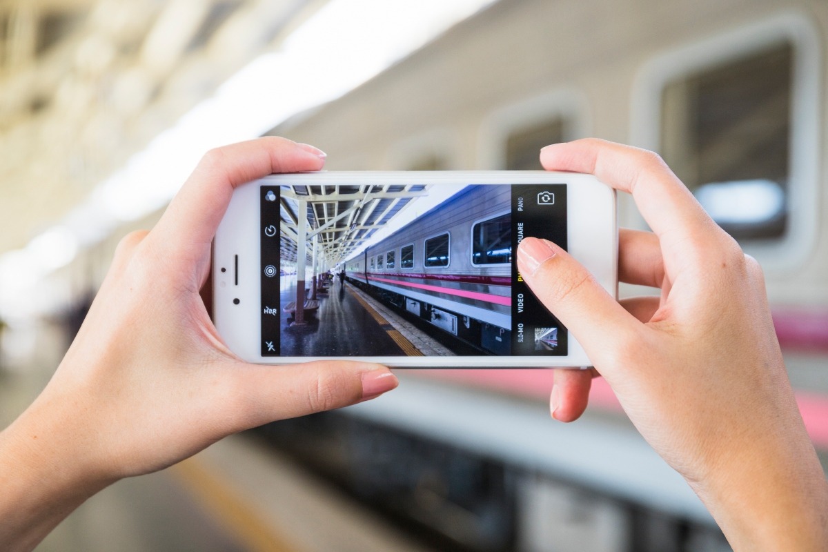 Hands holding a phone and taking photos of a train station.